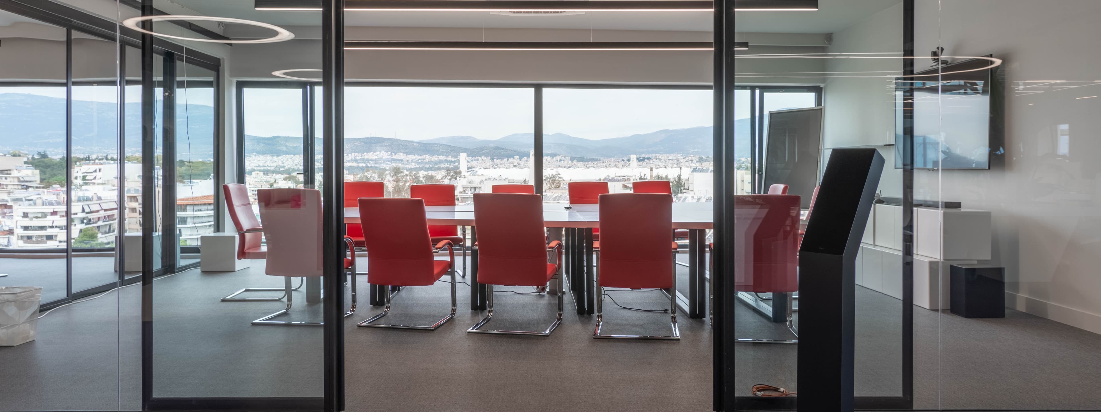 An ATCOM boardroom with red chairs and a floor-to-ceiling city and mountain view