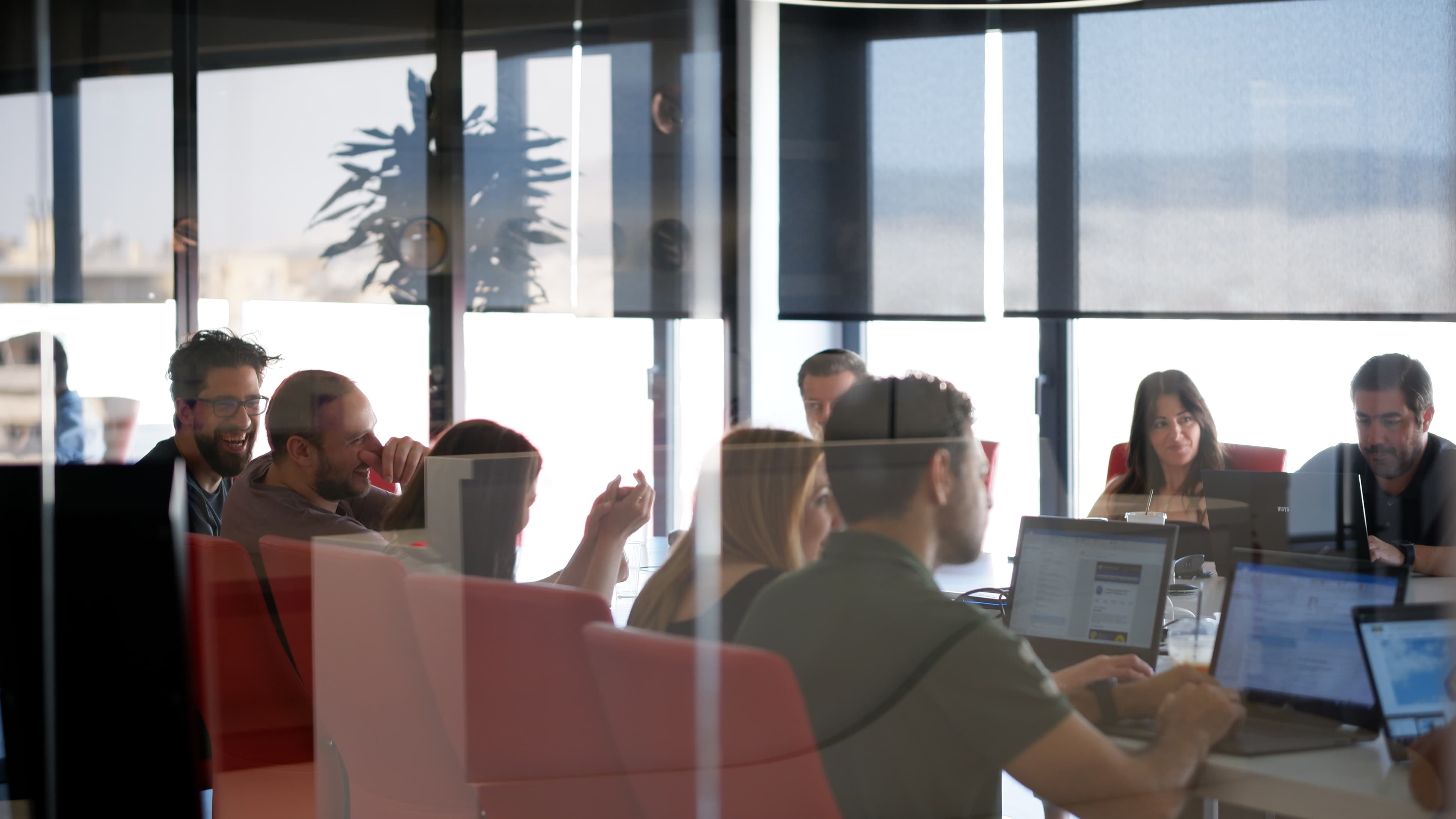 ATCOM team collaborating at their desks in a glass-walled office with a city view