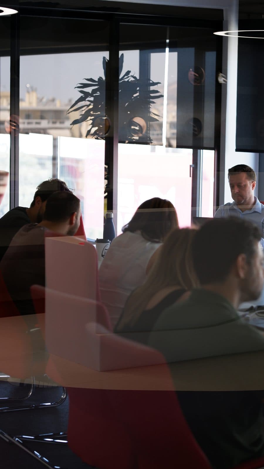 An ATCOM team meeting around a table by the office windows